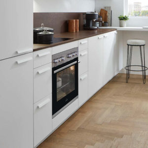 Einbaugeräte in einer weißen Küche mit dunkelbrauner Arbeitsplatte.