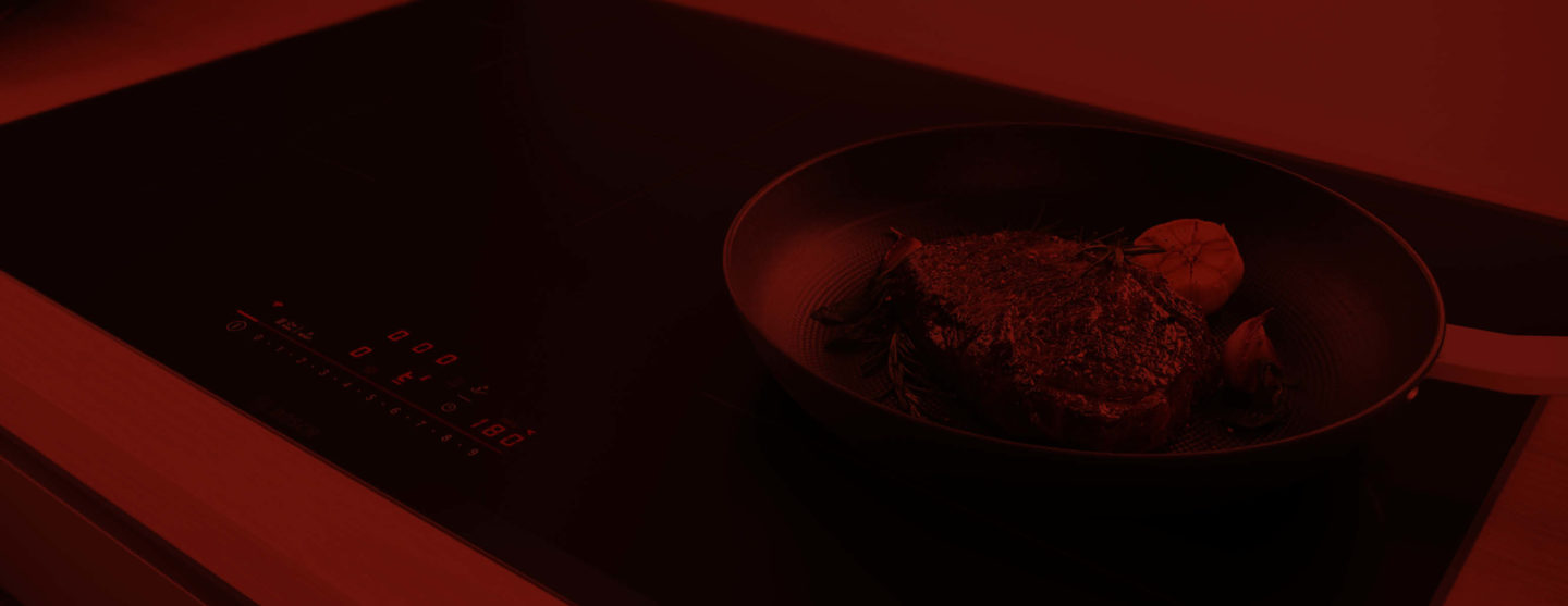 Induktionskochfeld mit Pfanne mit Steak und Knoblauch darauf – Elektrogeräte in Marl