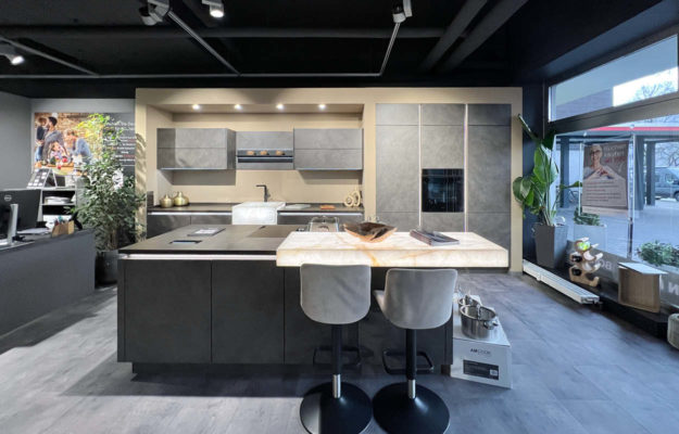 Moderne, grifflose Küche in Schieferoptik mit Kochinsel, beleuchteten Elementen und Kehlleistenbeleuchtung.