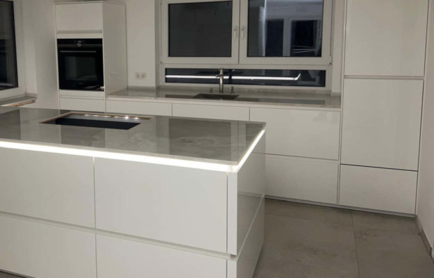 Weiße Küche mit Natursteinarbeitsplatte und beleuchteten Kehlleisten an der Kücheinsel