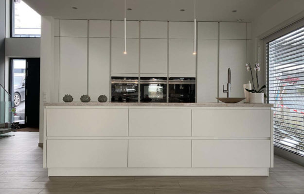 Moderne, weiße Küche mit Kochinsel und heller Steinarbeitsplatte.