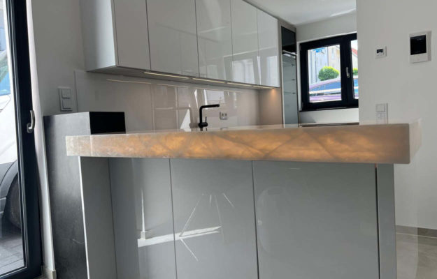 Moderne, weiße Hochglanzküche in L-Form mit leuchtender Arbeitsplatte.