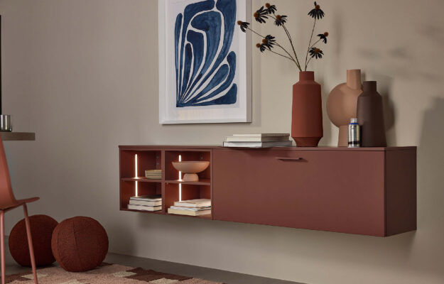 Nolte Wohnmöbel in warmem Hennarot mit integrierter Beleuchtung, stilvollen Dekoelementen und klarer Linienführung für ein modernes, wohnliches Ambiente